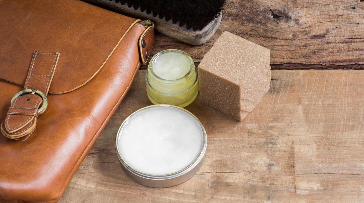 Sandale en cuir noir partiellement immergée dans une bassine d'eau savonneuse, avec une éponge naturelle et un pain de savon glycériné sur le rebord